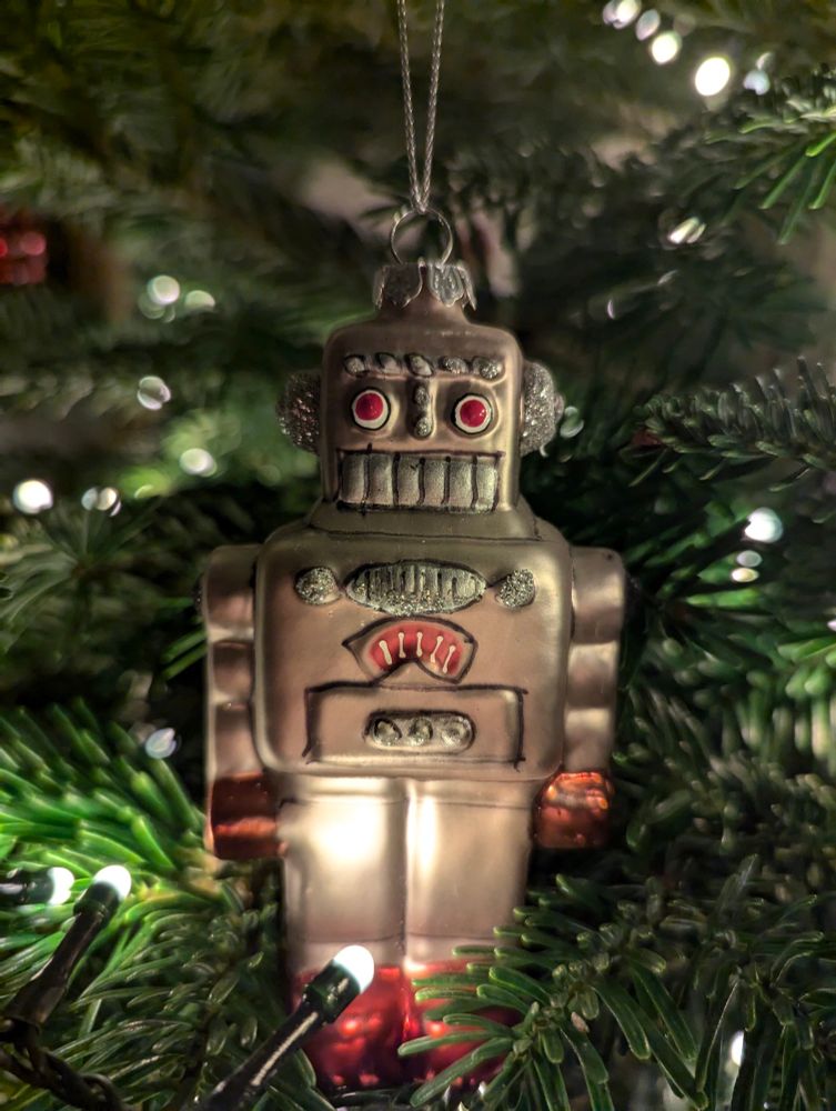 A Christmas decoration shaped like a silver robot, hanging on a tree 