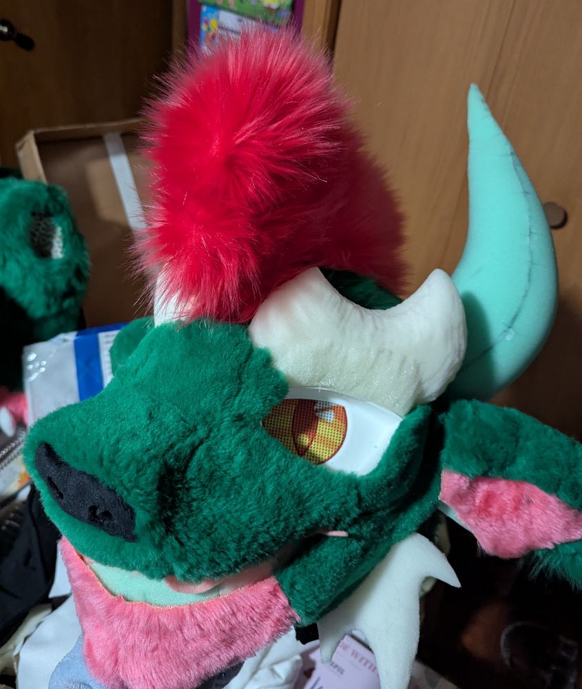 A hodag fursuit head partially furred. The cheek fluff, horns, and eyebrows are not yet covered.