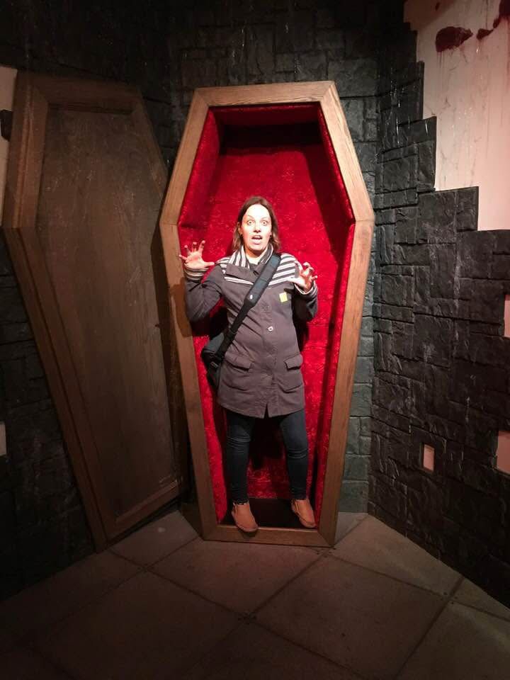 Woman, making a scary jesture, standing in a large open coffin. The coffin is lined with what looks like red velvet.

I shall neither confirm nor deny that this person is me!!