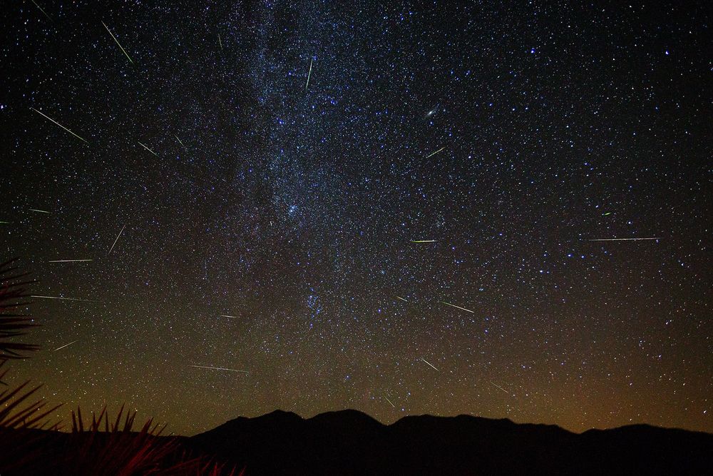 Starry night sky with several meteors streaking outward from the centre. Most meteor trails have a gradient, transitioning from green to yellow.
