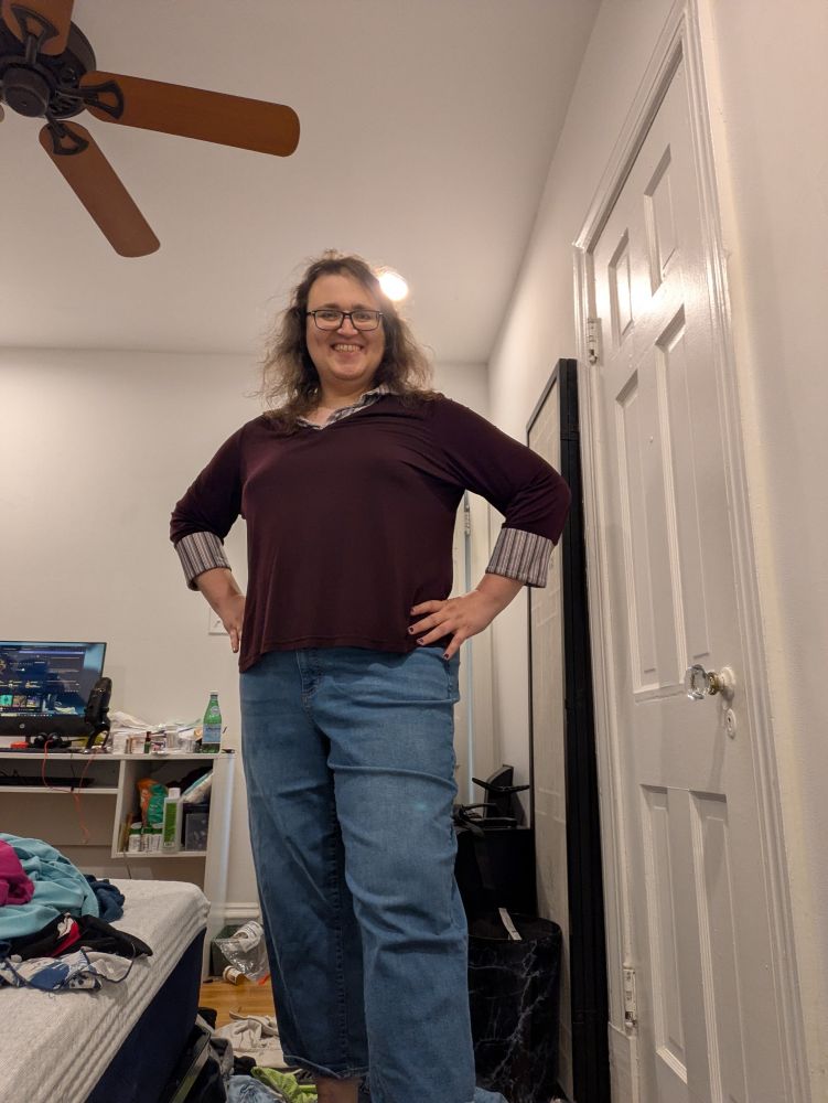 Woman in jeans and a burgundy shirt with striped cuffs and collar posting