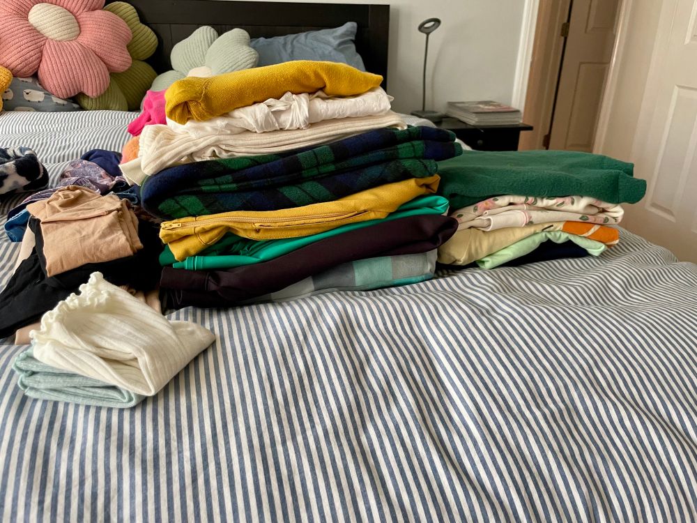 Piles of clothes on a bed. There is an over abundance of green and gold items. 