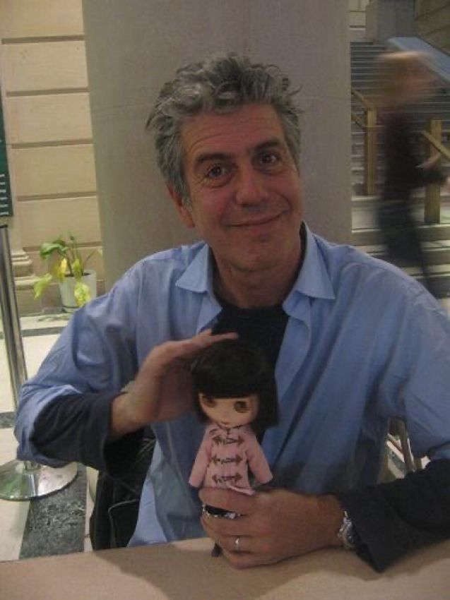 anthony bourdain holding a blythe doll in a pink button jacket