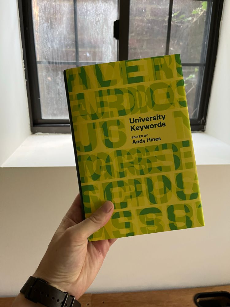 a hand holding a copy of a green and yellow book: University Keywords, edited by Andy Hines 