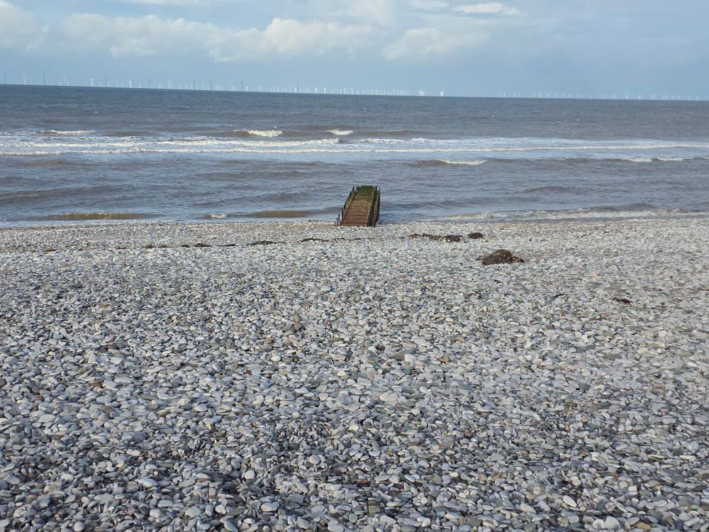A shale beach with small waves crashing. Some sort of weird ladder structure in the middle.