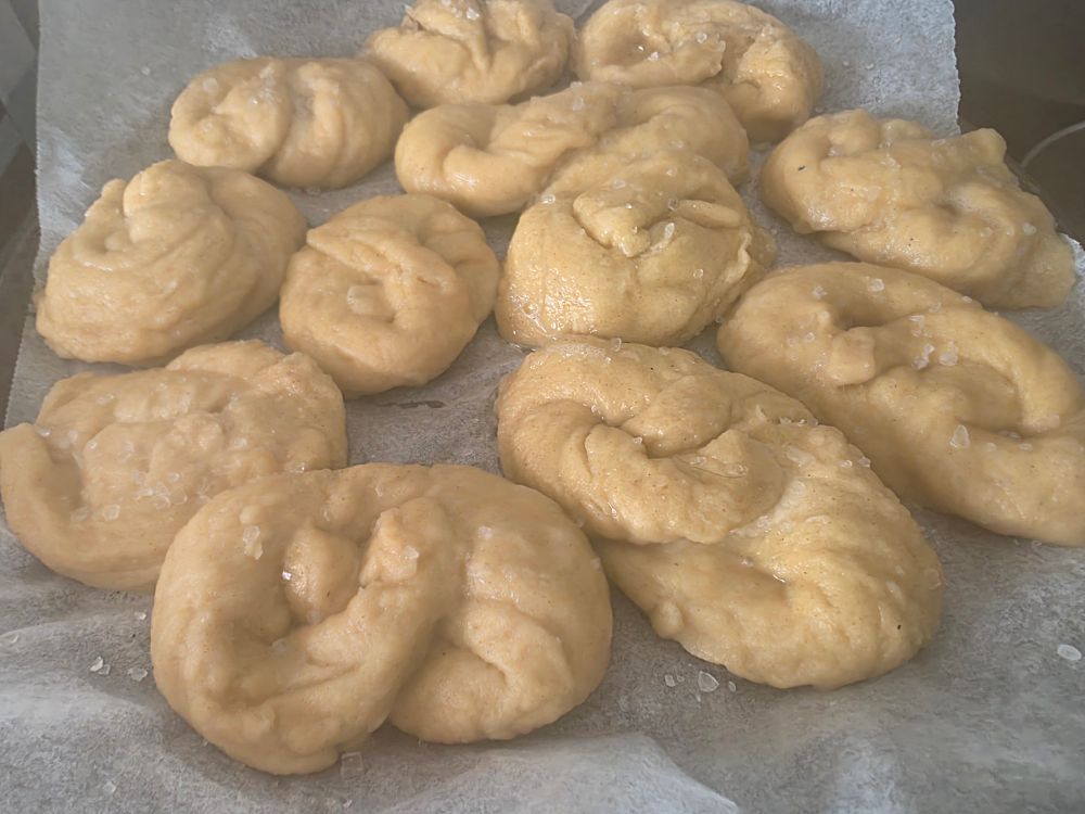 Uncooked sourdough pretzels on a baking tray covered on sea salt.