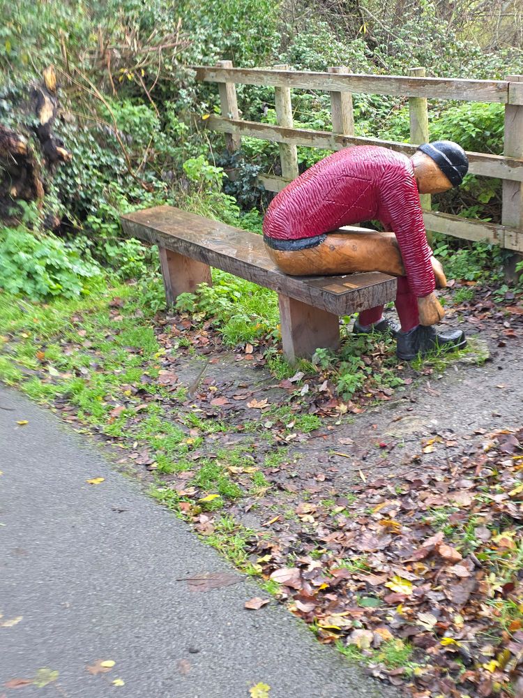 A wooden man tying his shoe on a bench.