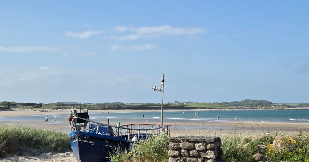Blue sky, beach and sea with a navy wooden boat in the foreground