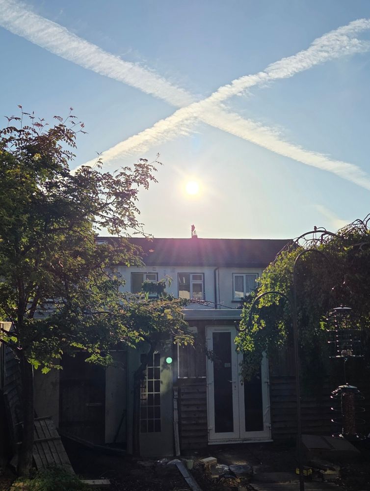 Clear blue Sky with airplane contrails  making a crisscross x shape above the sun. 