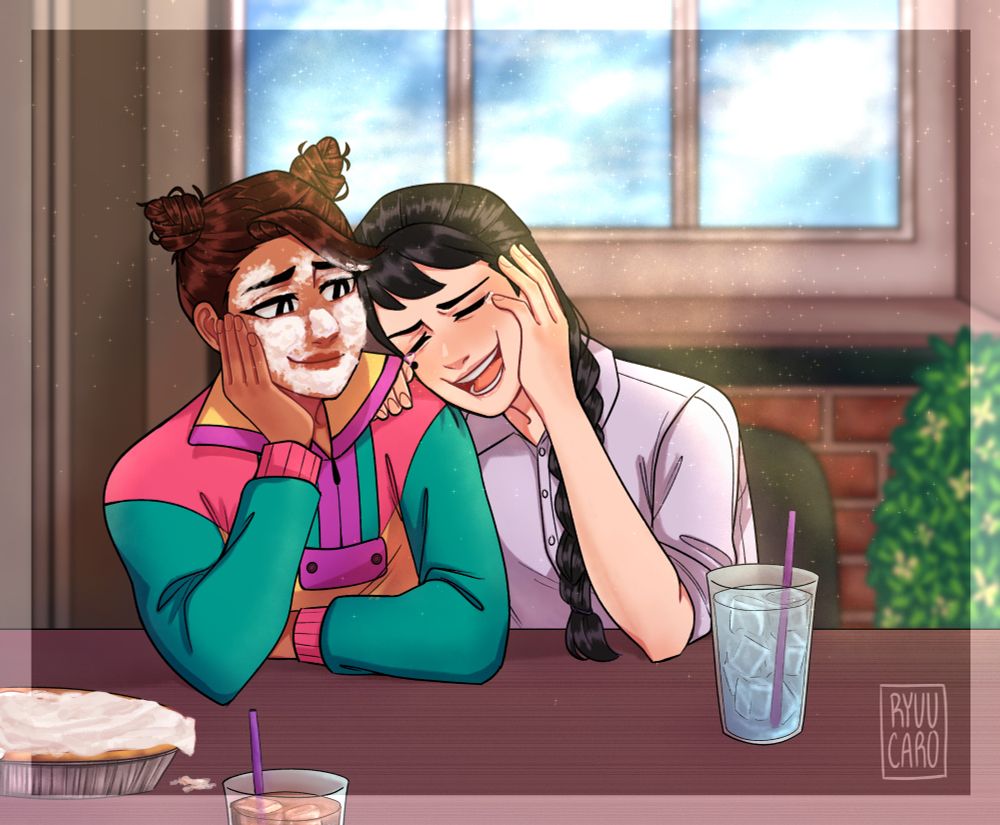 Akarsha sits beside Noelle, looking lovingly at her and leaning her face on her hand as Noelle laughs so hard she's leaning onto Akarsha. They sit at a restaurant, drinks in front of them and a pie off to the side of the table. Akarsha's face is covered in said pie, presumably due to a prank on Noelle's part. 