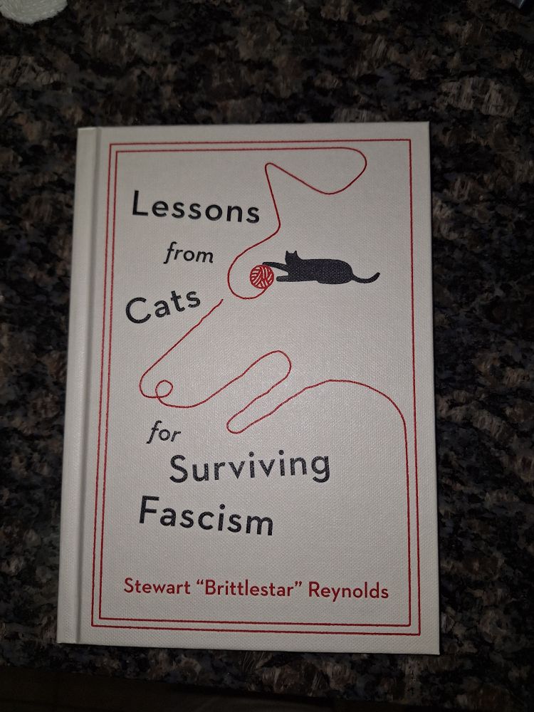 A mostly white hardcover book entitled "Lessons from Cats for Surviving Fascism", by Stewart "Brittlestar" Reynolds.