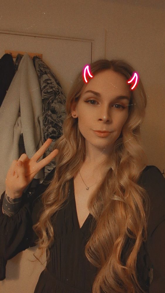 long haired blonde trans girl with devil horns throwing up a peace sign