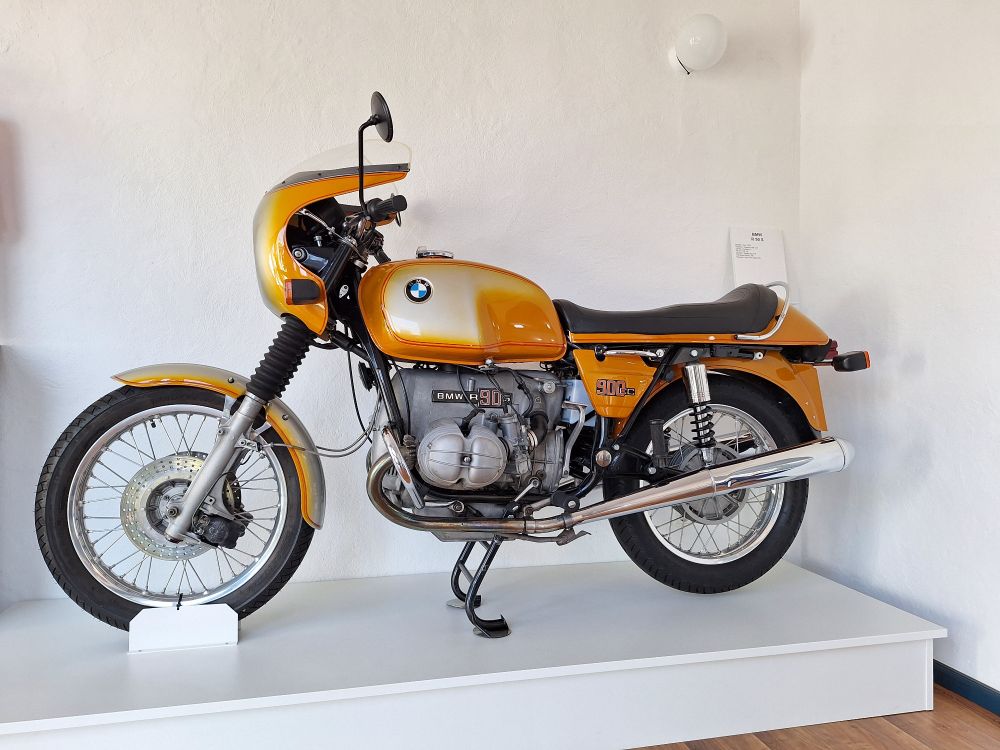 Foto zeigt ein älteres Motorrad aus den 70ern mit Boxermotor in Silber. Speichenfelgenund reichlich Chrom. Schutzblech, die kleine Halbschale am Lenker sowie Tank, Seitenbleche und Heck samt Schutzblech hinten sind Orange lackiert.