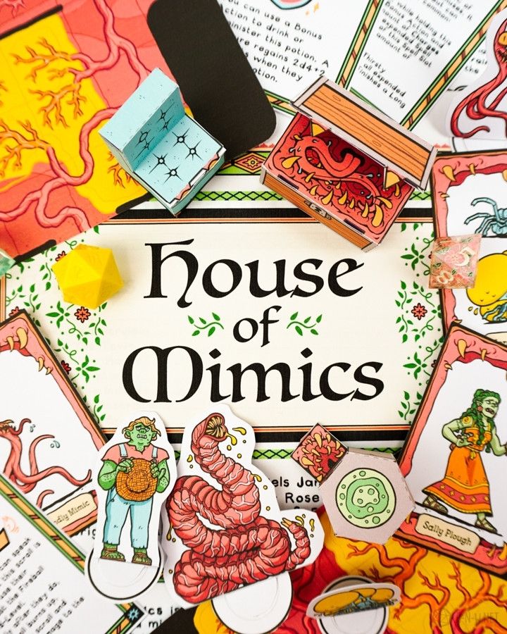 A photograph displaying various elements from the House of Mimics adventure, including character cards, paper minis, papercraft minics, and a logo