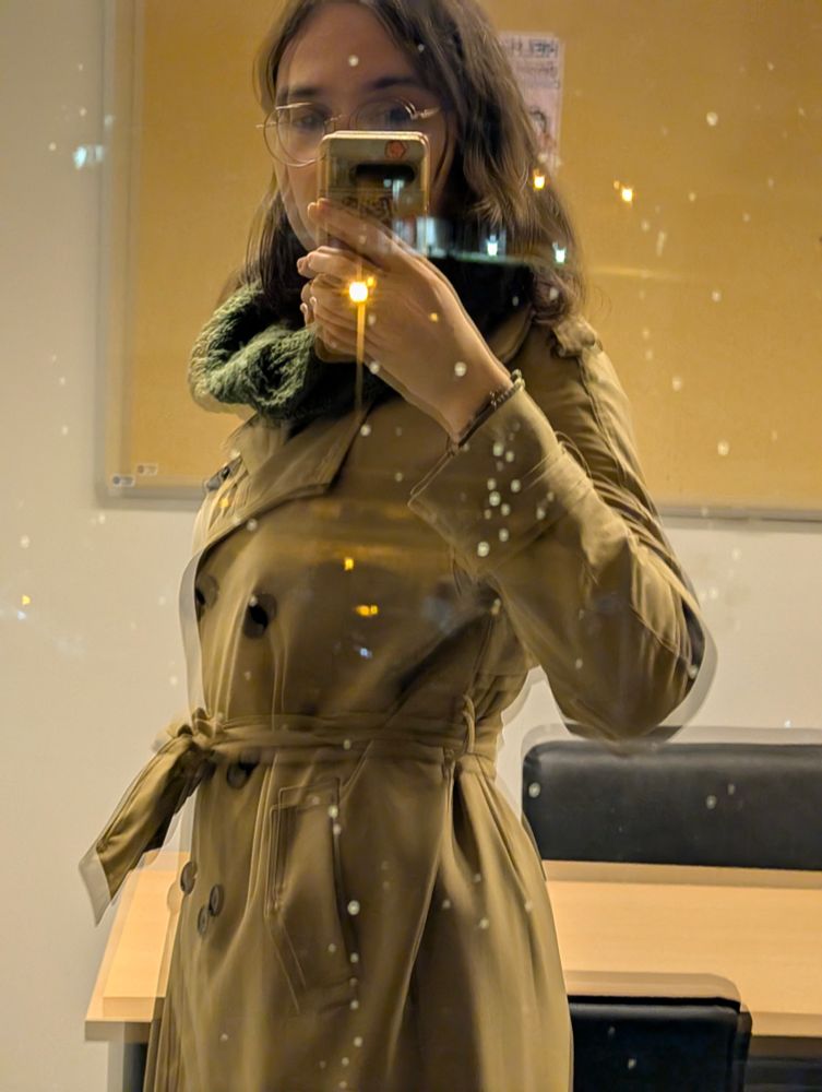 photo of a window at night partially showing city lights outside and partially reflecting my own image. the brightest light is right on my hand