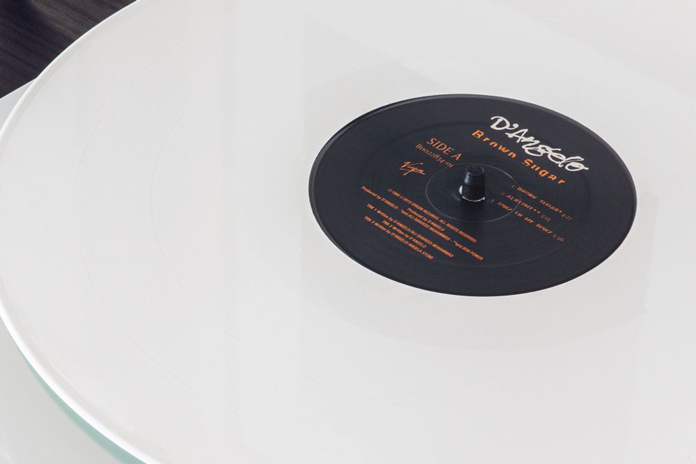 Close up of Brown Sugar by D’Angelo, vinyl album, on a turntable. White vinyl with black center label with brown text, and artist name in stylized white text. Photograph by thetrudz.