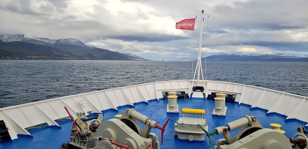 A ship's bow sailing out of the Beagle Channel under moody clouds