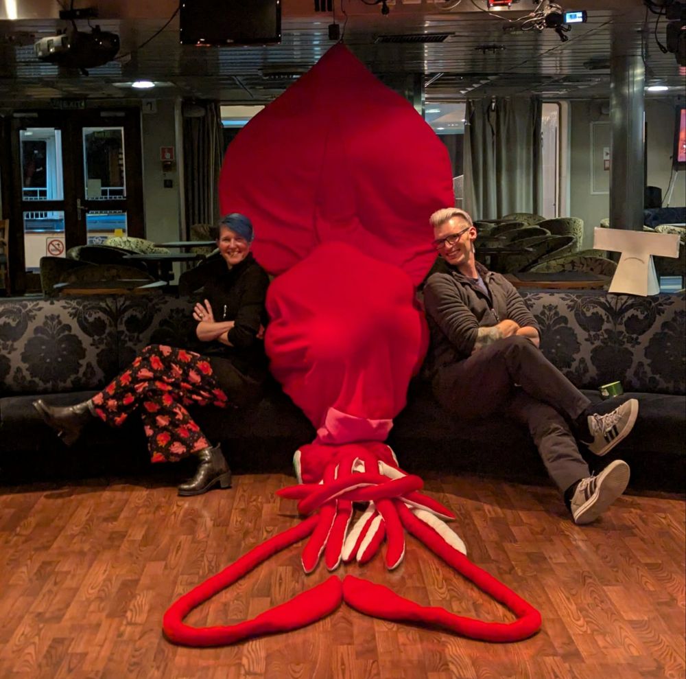 Two scientists and a full-sized stuffed colossal squid on a couch aboard a ship