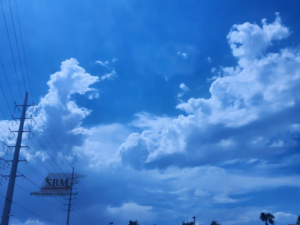 An overlay of blue light over cumulus clouds on a bold blue sky