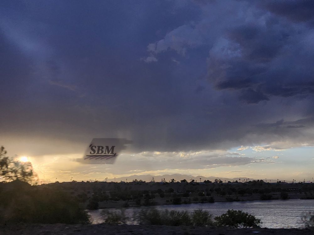 Deep blue gray cumulus, stratocumulus, and cumulonimbus clouds before a pale yellow sky over a calm pond