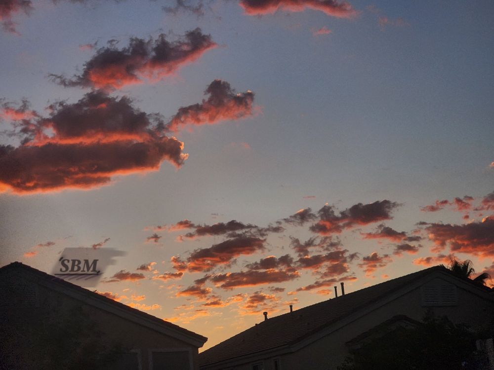 Red lit gray stratocumulus clouds on a light blue sky with a small golden glow above the set sun