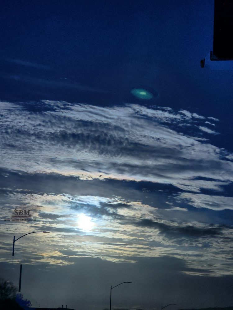 A moody deep blue sky with the sun being filtered through stratocumulus and altocumulus clouds, creating a yellow illuminated ring