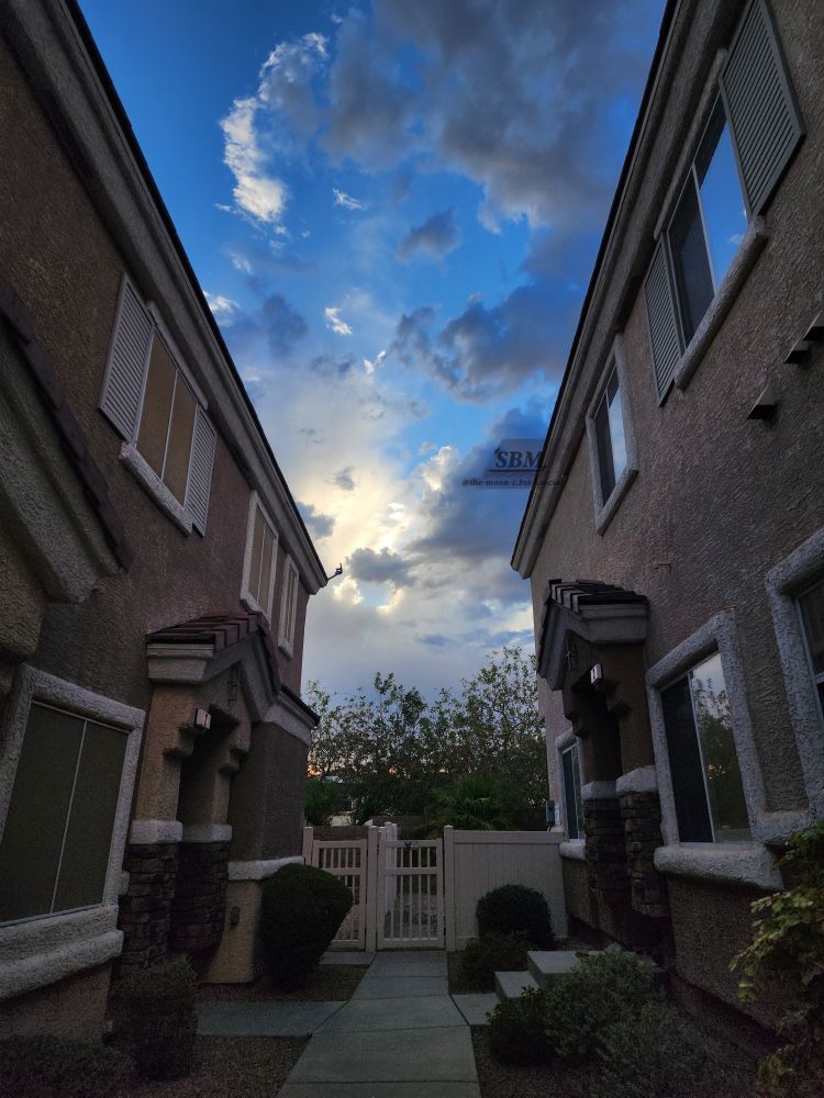 An inviting bright blue sky behind cumulus clouds of varying color at sunrise inbetween two buildings
