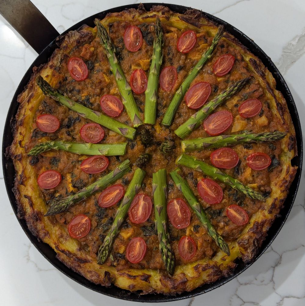 Top-down view of red-pepper lentil pie with a mashed potato crust. A asparagus is in a circular arrangement on top.