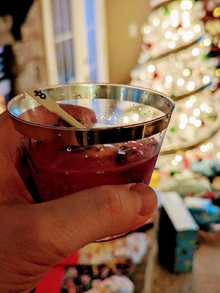 Drink in the foreground with a white Christmas tree out of focus in the background.