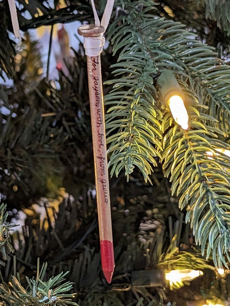 A wood nail with the tip dipped in red paint. "For Jayson, with love, from Jesus" written on the side. It is attached with a ribbon to a Christmas tree.