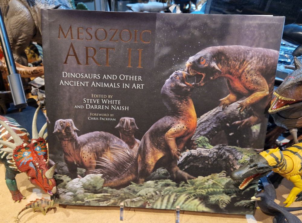 Mesozoic Art II, the book, on a cluttered desk with dinosaur toys. 