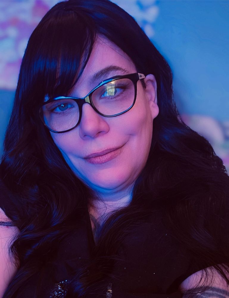 Emm with black hair, bangs, and glasses in a black shirt smirking at you. 