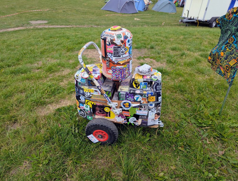 The World of Techno wheeled speakers and electronics covered in stickers from many years of hacker camps sitting on top of a small hill waiting to be taken for a walk