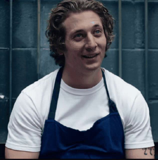 a man wearing a blue apron and a white shirt has a tattoo on his arm that says 22