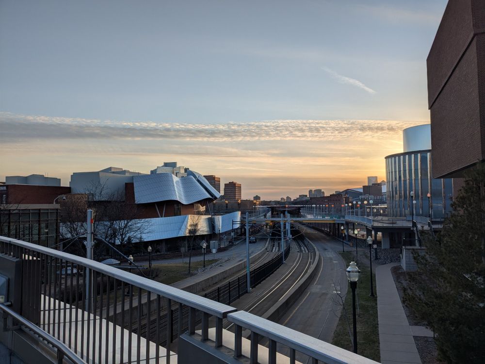 Sunset from the East Bank campus last night, with a view of an art museum and train tracks running across the Mississippi. A thin (cirrus?) cloud cuts across horizontally.