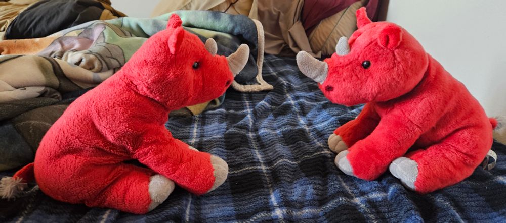 Two red rhino plushies staring at each other.