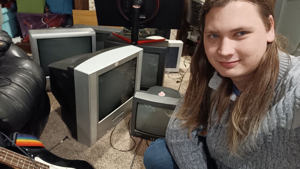 Similar to the last photo but at a much lower angle, only 6 of the TVs are visible and I'm crouching and smiling in frame