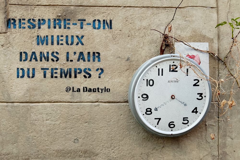 Une horloge indiquant 15h40 accrochée à un mur où poussent quelques brindilles. A côté un pochoir de @LaDactylo demande "Respire-t-on mieux dans l'air du temps ?"