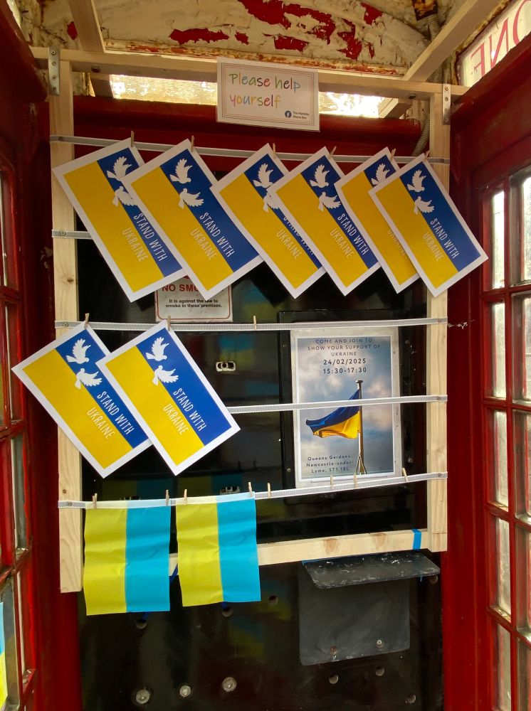 A photograph showing the display inside the red telephone box, with Ukrainian flags and printed sheets saying ‘Stand with Ukraine’, free for the public to take away. 