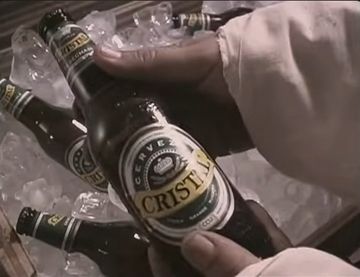 Two hands holding a Ceveza Cristal beer over a full ice chest 
