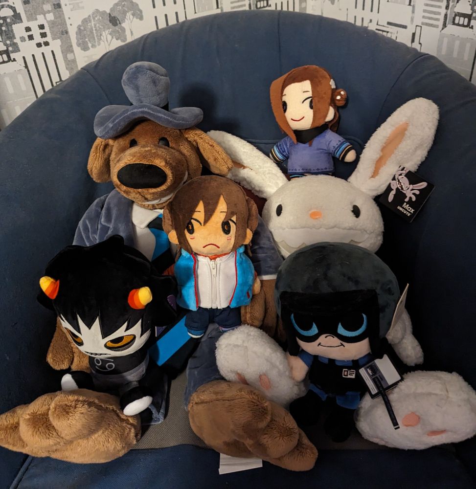 A picture of multiple plushies sitting on a blue armchair. The plushies are Sam and Max (much bigger than the rest), Karkat from Homestuck, Junpei and Akane from Zero Escape and Benrey from Half Life vr but the ai is Self-aware. Karkat is sitting in Sam's lap and Junpei is standing on Sam's other leg. Benrey is sitting in Max' lap and Akane is standing on his head.