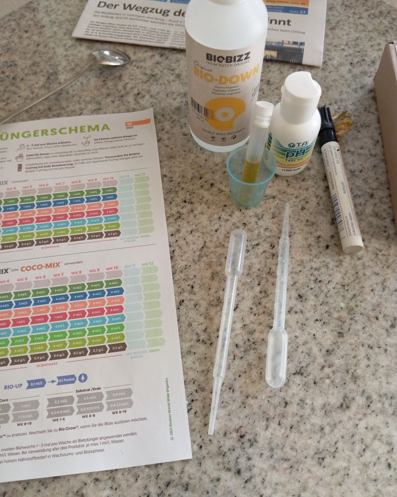 Auf einem Tisch liegen neben einer Tabelle "Düngerschema", Pipetten, ein Reagenzgläschen mit grüngelber Flüssigkeit und Chemiefläschen um den ph Wert von Wasser zu bestimmen und zu verändern.