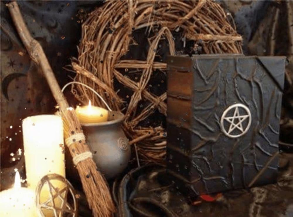a book with a pentagram on it sits on a table next to candles and a broom