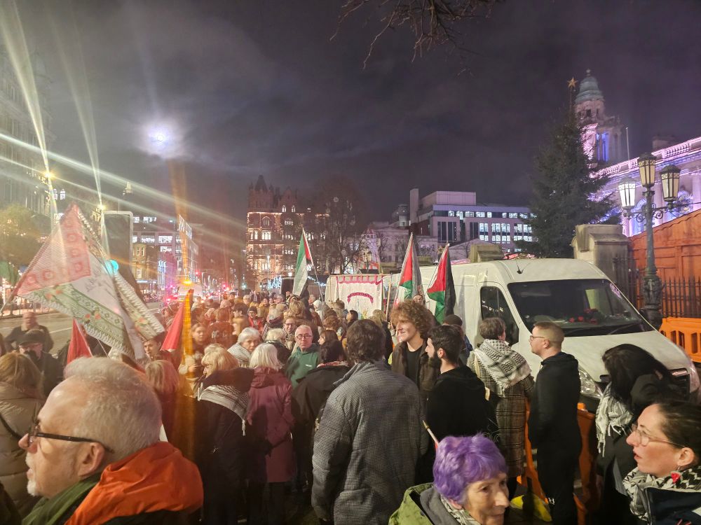 A crowd packed on a footpath with Palestinian flags