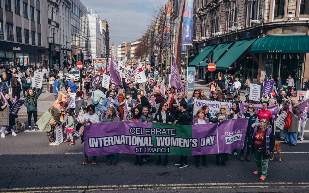 Photo of the IWD banner arriving at Belfast city hall, the rest of the march stretches off down the road in the background. 