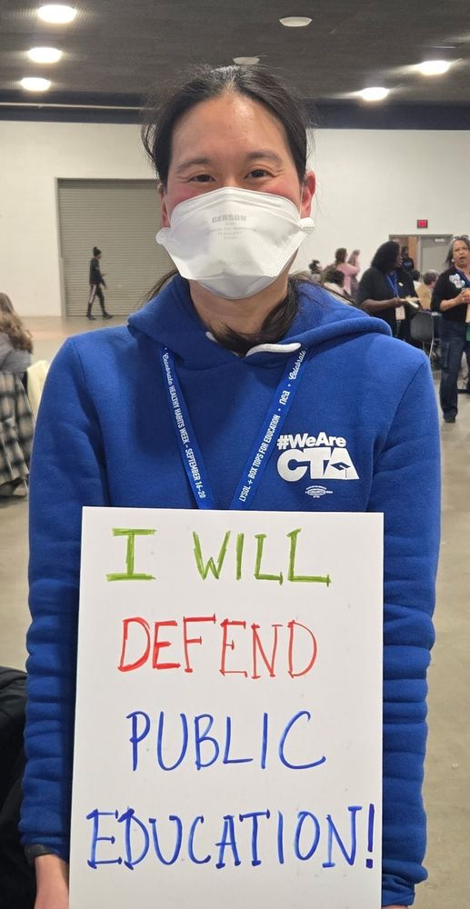 OP holding a sign that reads "I will defend public education"