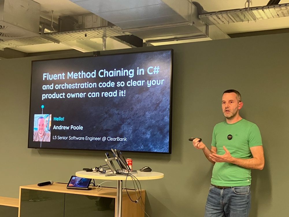 A guy in a green shirt talking about code. Next to him is a large screen showing the text “Fluent Method Chaining in C#”