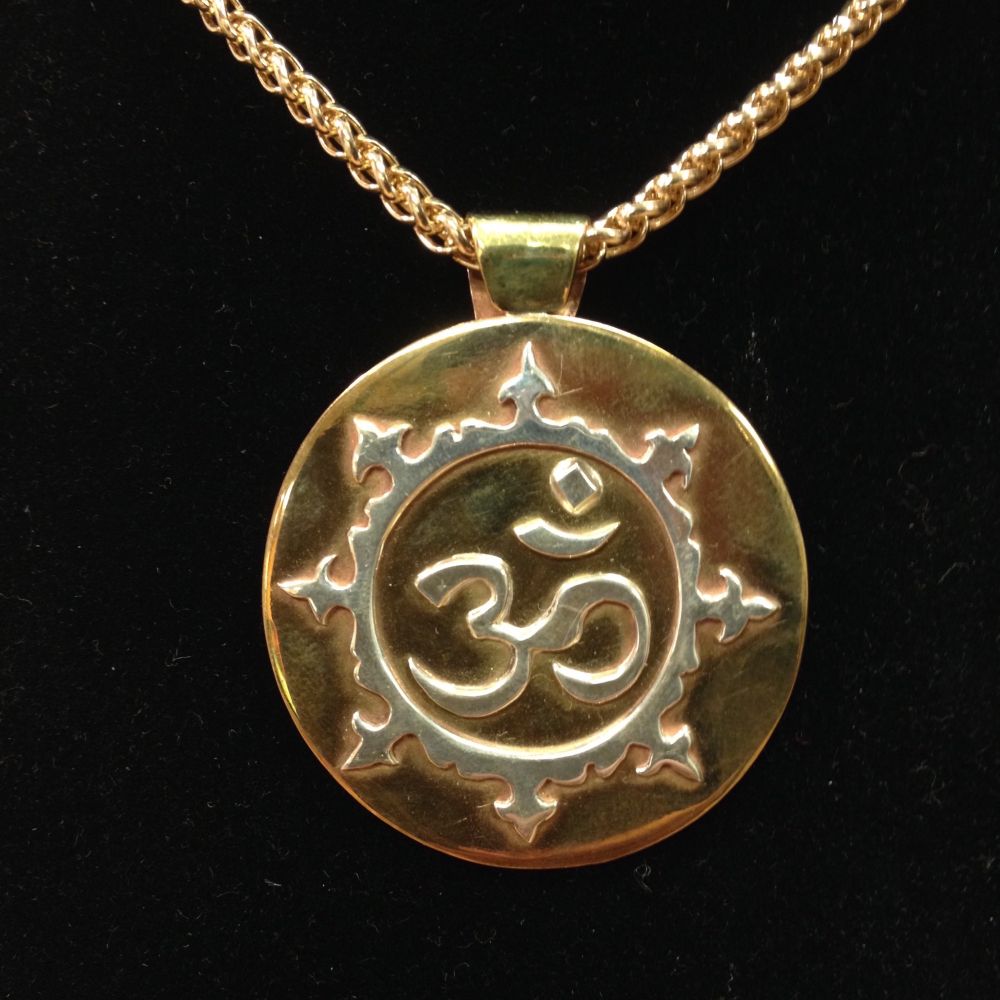 An adorned “Ohm” symbol in Devanagari script in silver, on a brass circle backing with brass chain