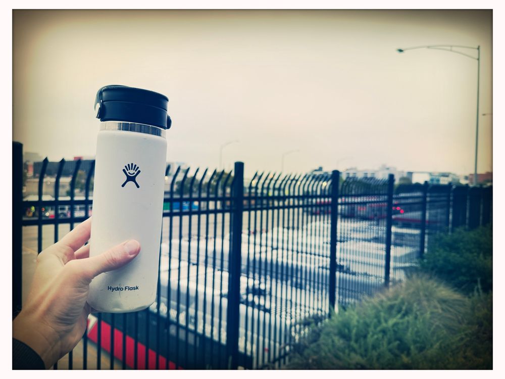 Travel coffee mug in front of fenced bus yard