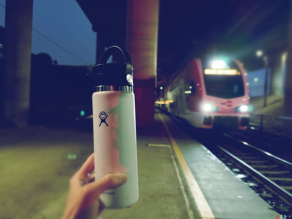 Travel coffee mug held up in front of an incoming Caltrain at 22nd Street